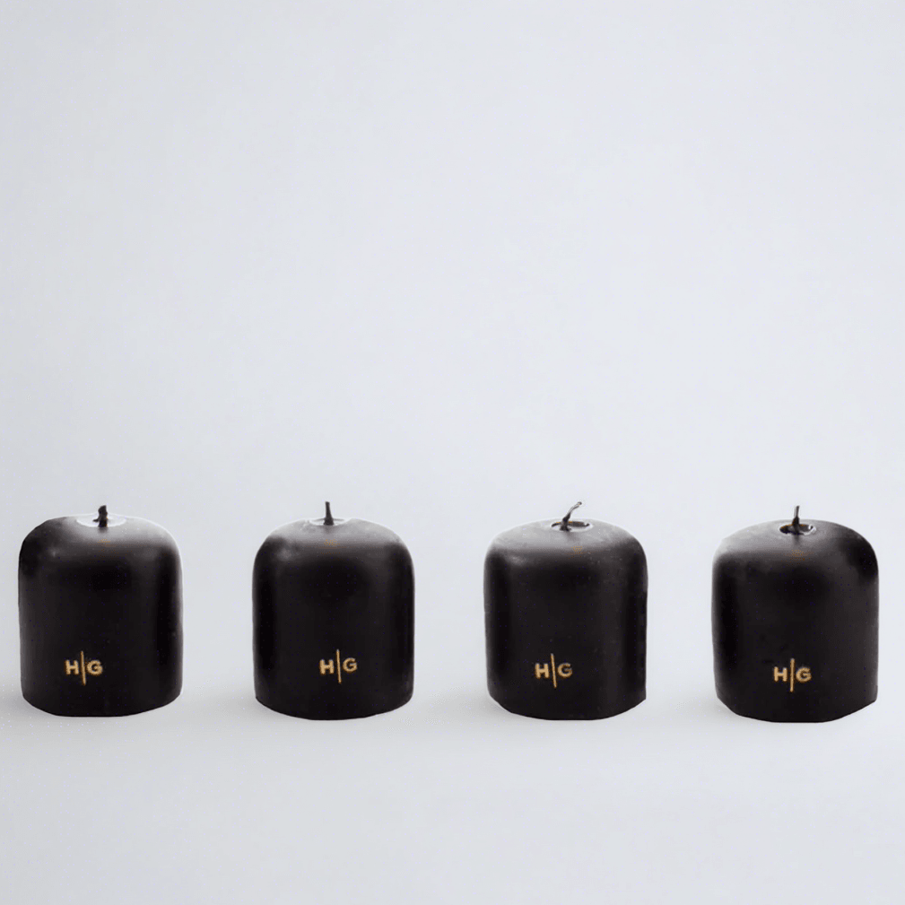 Four black unscented 2" votive candles with gold HG logo, made from paraffin and amber tree resin.