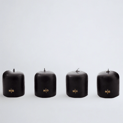Four black unscented 2" votive candles with gold HG logo, made from paraffin and amber tree resin.