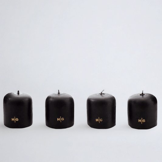 Four black unscented 2" votive candles with gold HG logo, made from paraffin and amber tree resin.