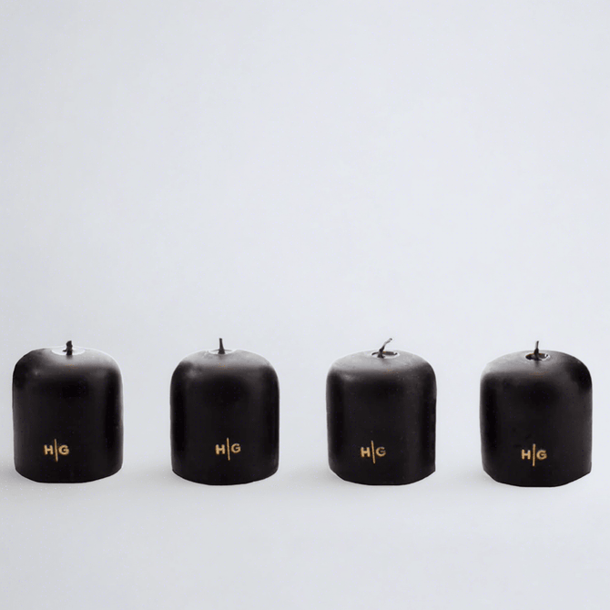 Four black unscented 2" votive candles with gold HG logo, made from paraffin and amber tree resin.