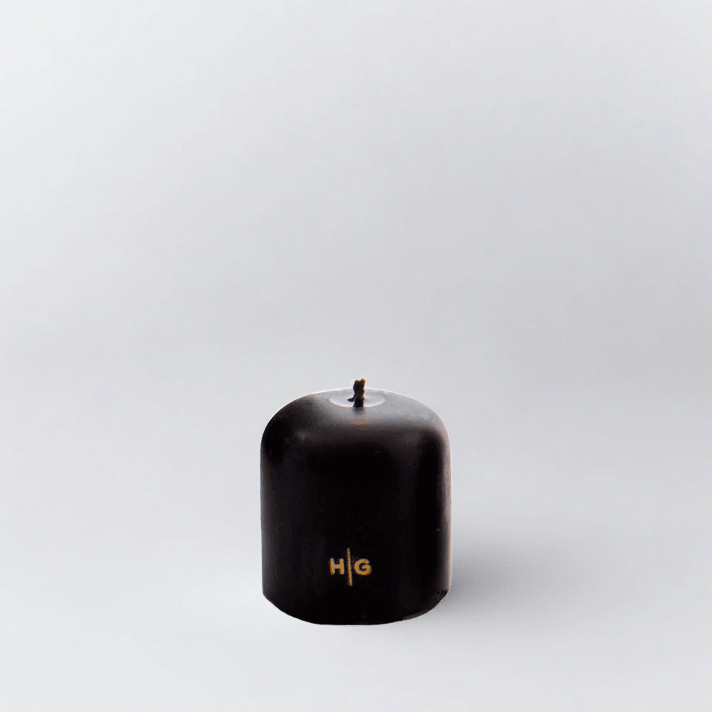 HG Black 3"x3" unscented pillar candle with gold embossed HG logo and oversized cotton wick.