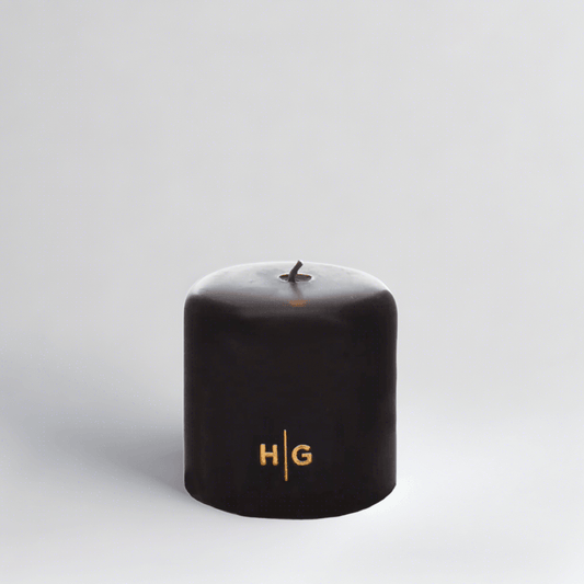 HG Black Unscented Pillar Candle, 4"x4", with gold embossed HG logo and oversized cotton wick.