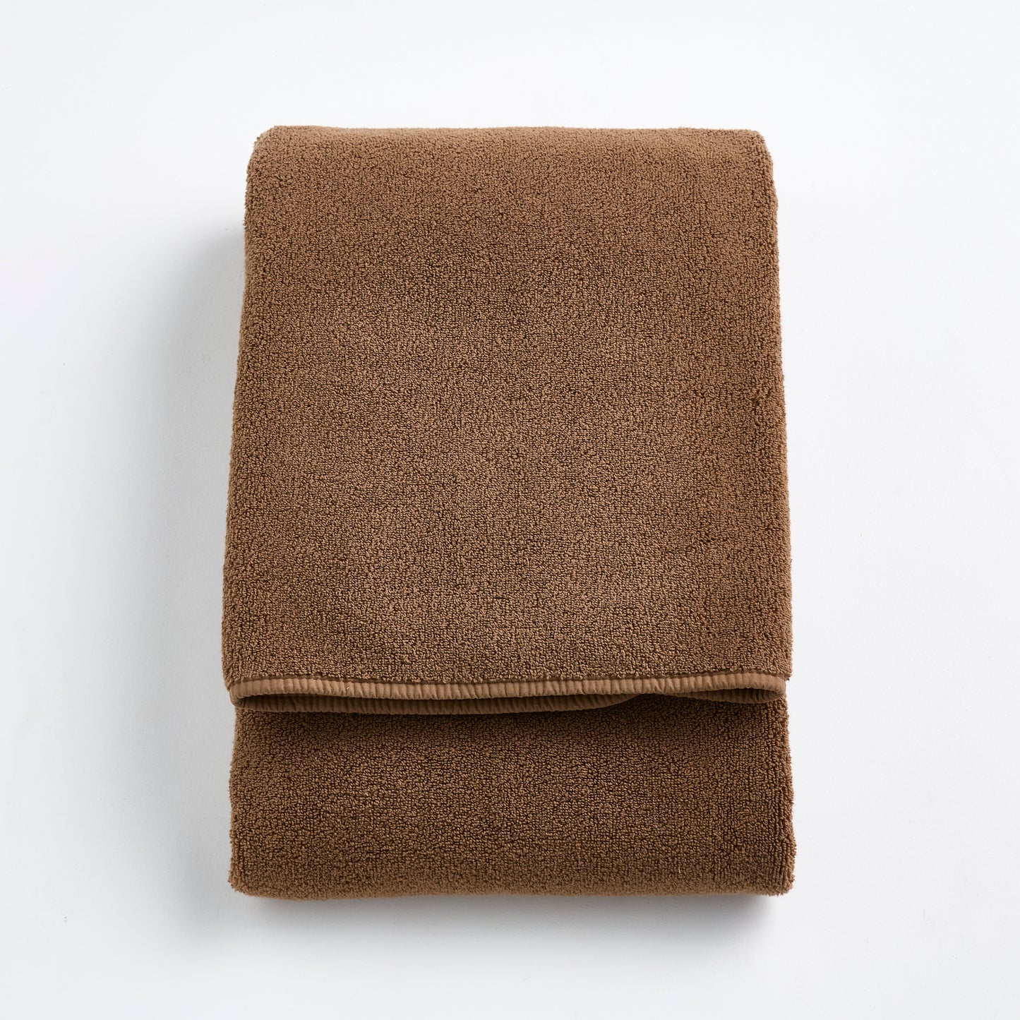 Folded coffee brown Signature bath towel made of soft, plush cotton terry fabric on a white background.