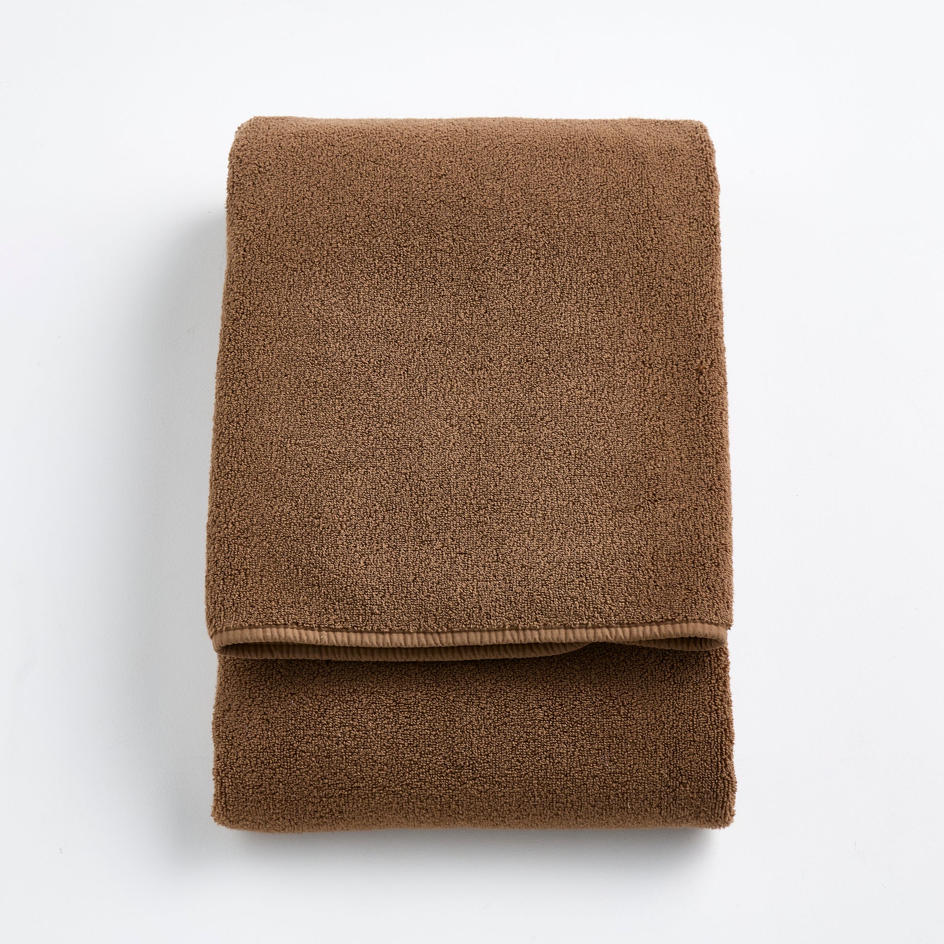 Folded coffee brown Signature bath towel made of soft, plush cotton terry fabric on a white background.