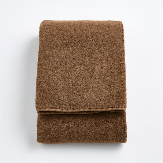 Folded coffee brown Signature bath towel made of soft, plush cotton terry fabric on a white background.