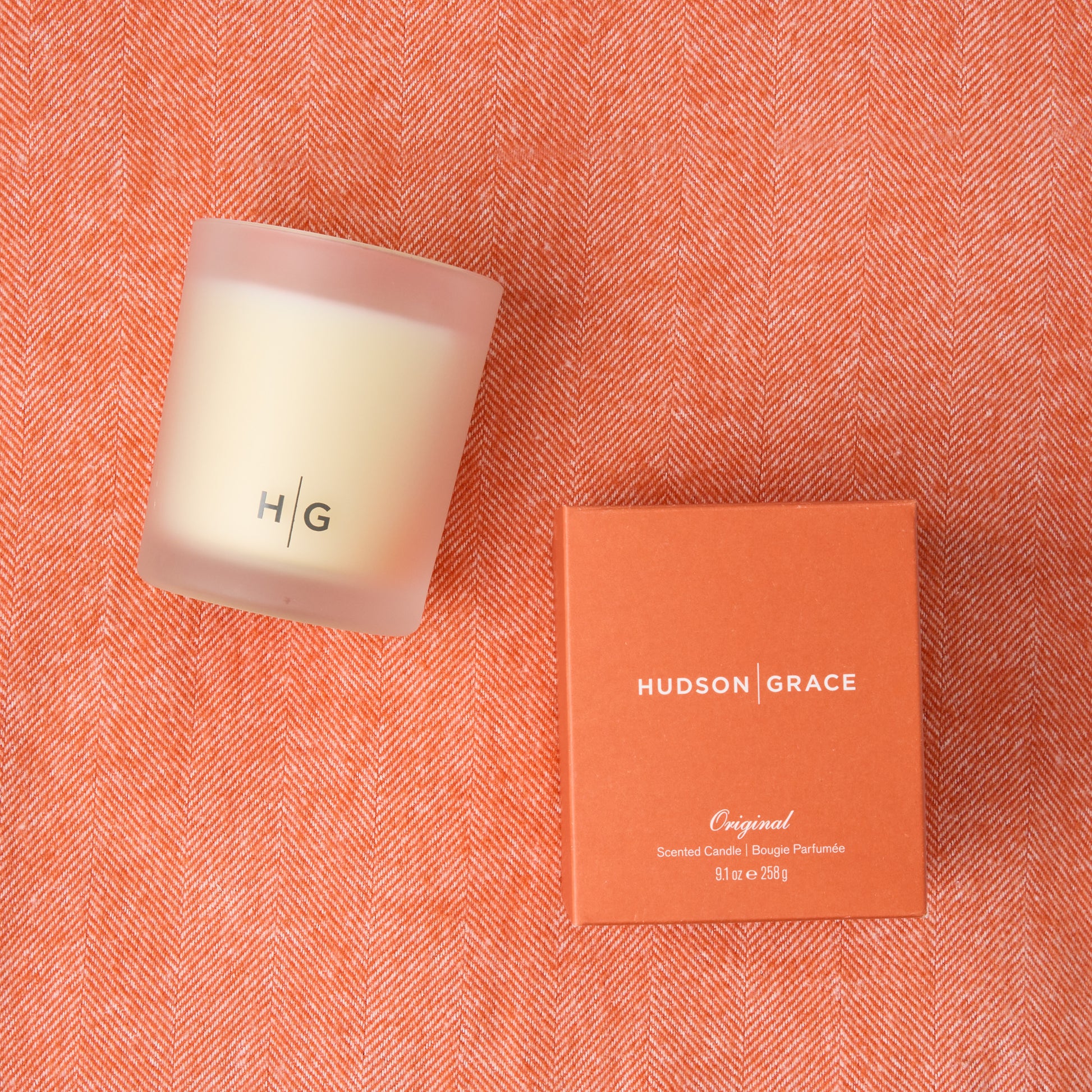 HG Original Scented Candle in frosted glass with orange box on a Mandarin Orange Italian Herringbone Throw.
