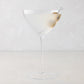 Oversized 14oz mouth-blown clear glass martini glass with a long stem and a single olive garnish.