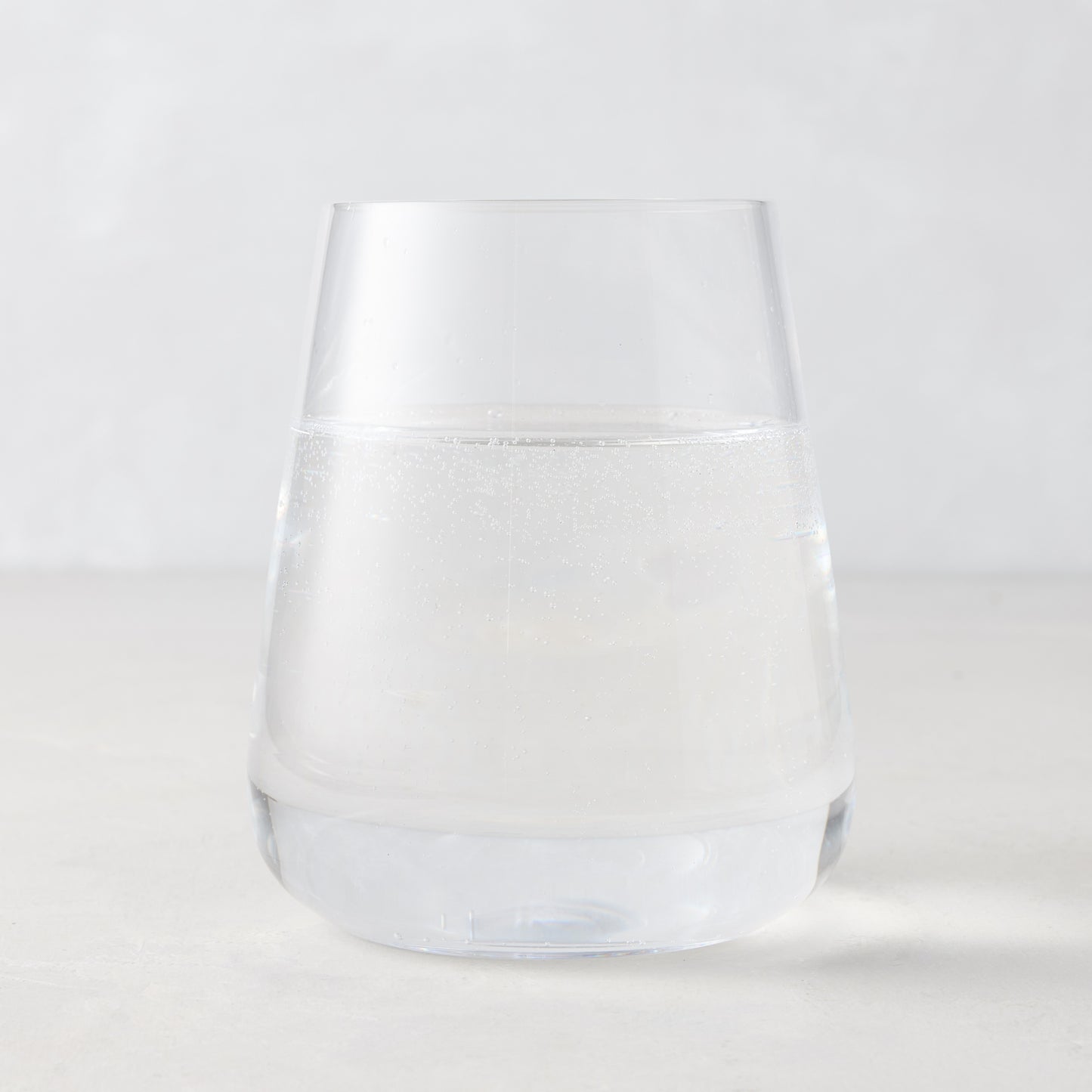 Clear HG Heritage Stemless Glass, mouth-blown, filled with water, on a light background.