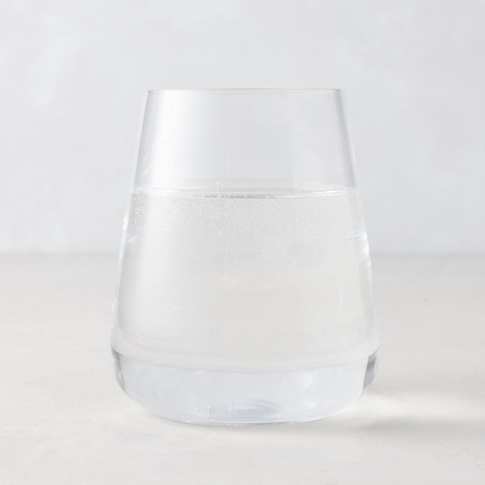 Clear HG Heritage Stemless Glass, mouth-blown, filled with water, on a light background.