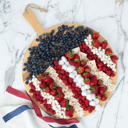 Round reclaimed wood serving board with handle, filled with blueberries, strawberries, raspberries, marshmallows, and nougat.