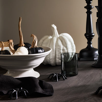 White ceramic footed bowl filled with black and white decorative pumpkins.