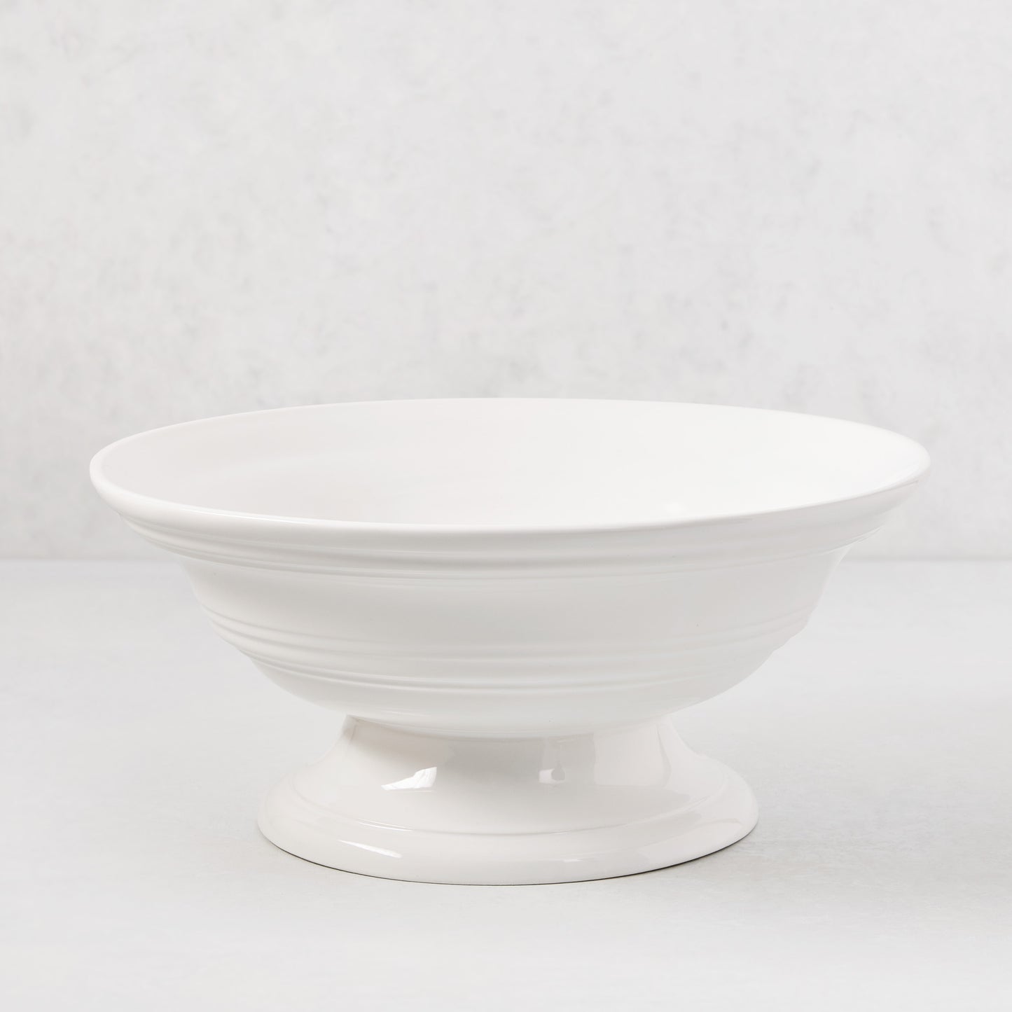 White ceramic footed bowl, 11.5" round, with a smooth glaze and subtle horizontal ridges.