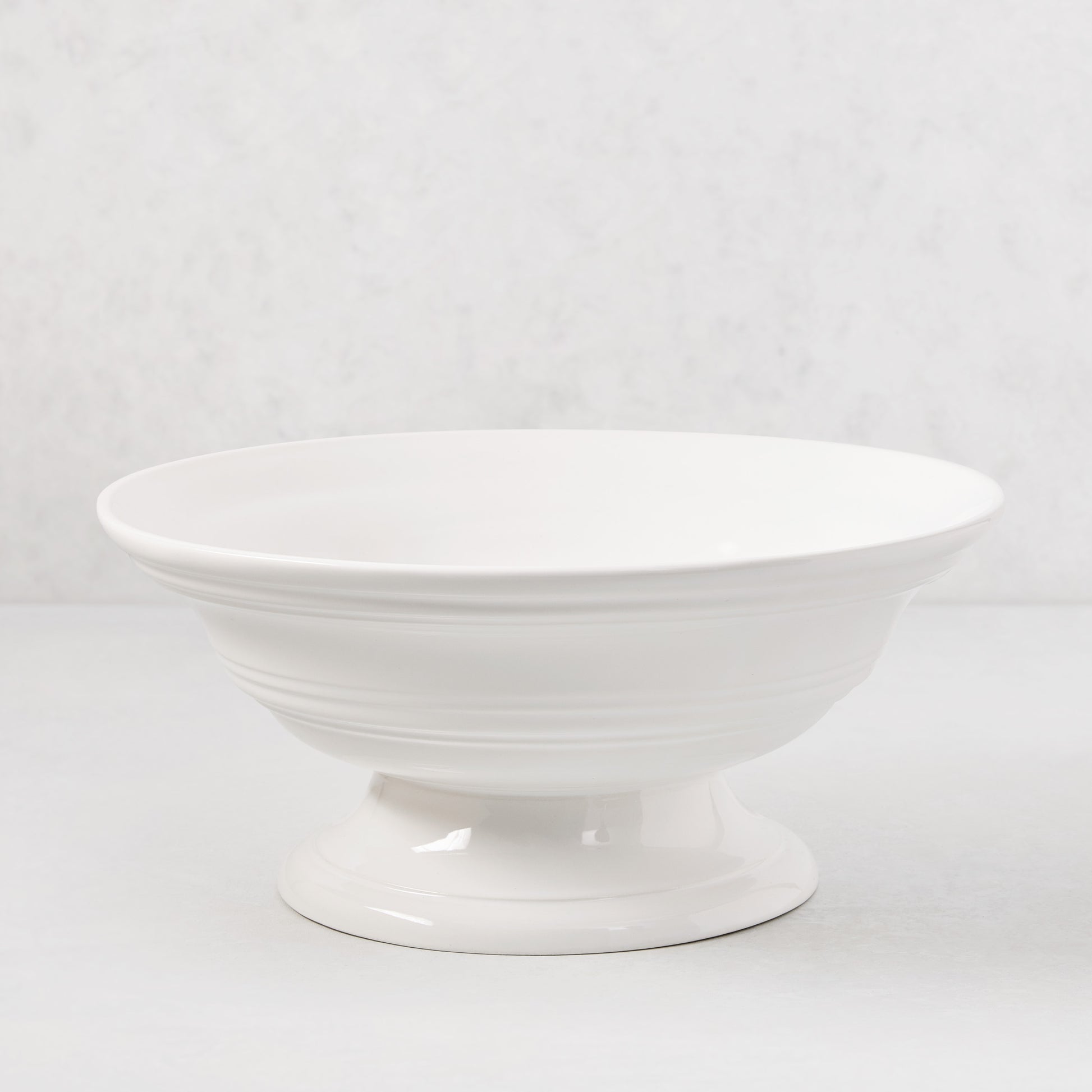 White ceramic footed bowl, 11.5" round, with a smooth glaze and subtle horizontal ridges.