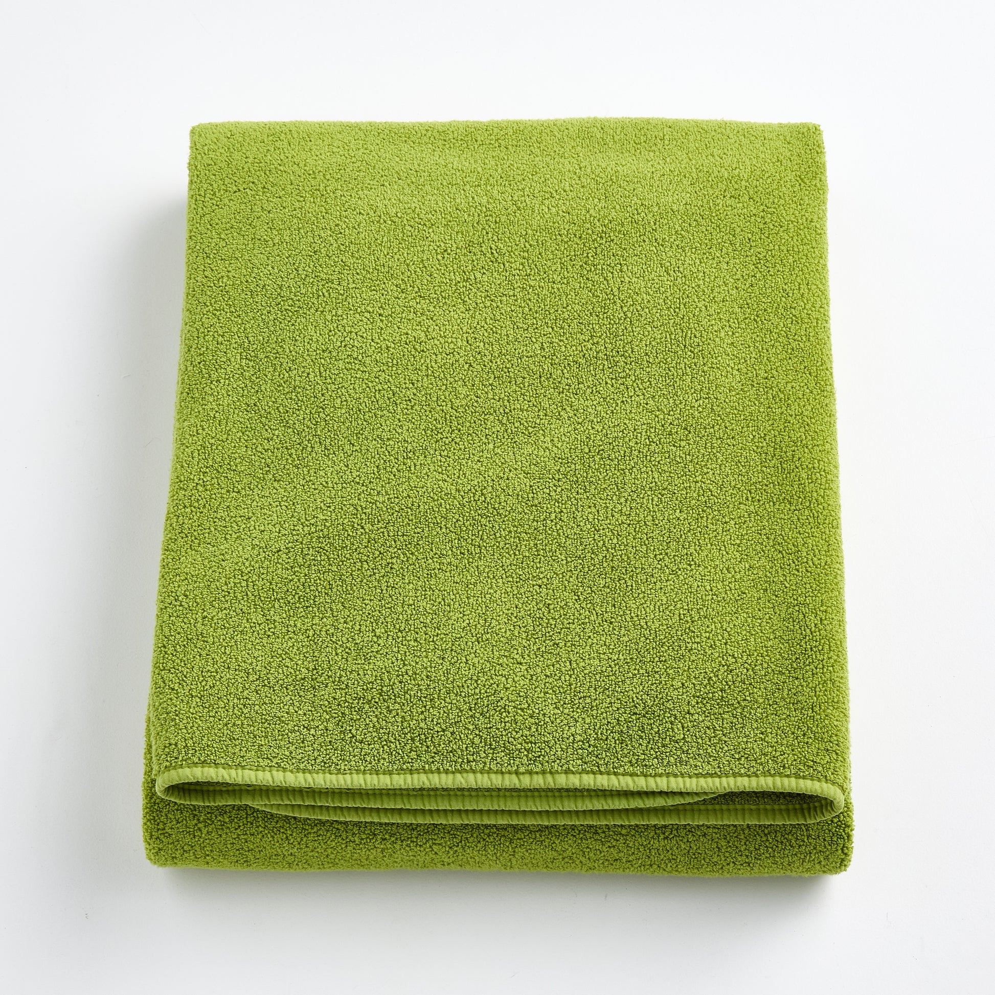 Folded aloe green bath sheet in zero twist cotton with matching bias piping, 40 by 70 inches.