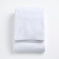 Folded cloud white signature bath towel made of plush, absorbent cotton fabric on a white background.