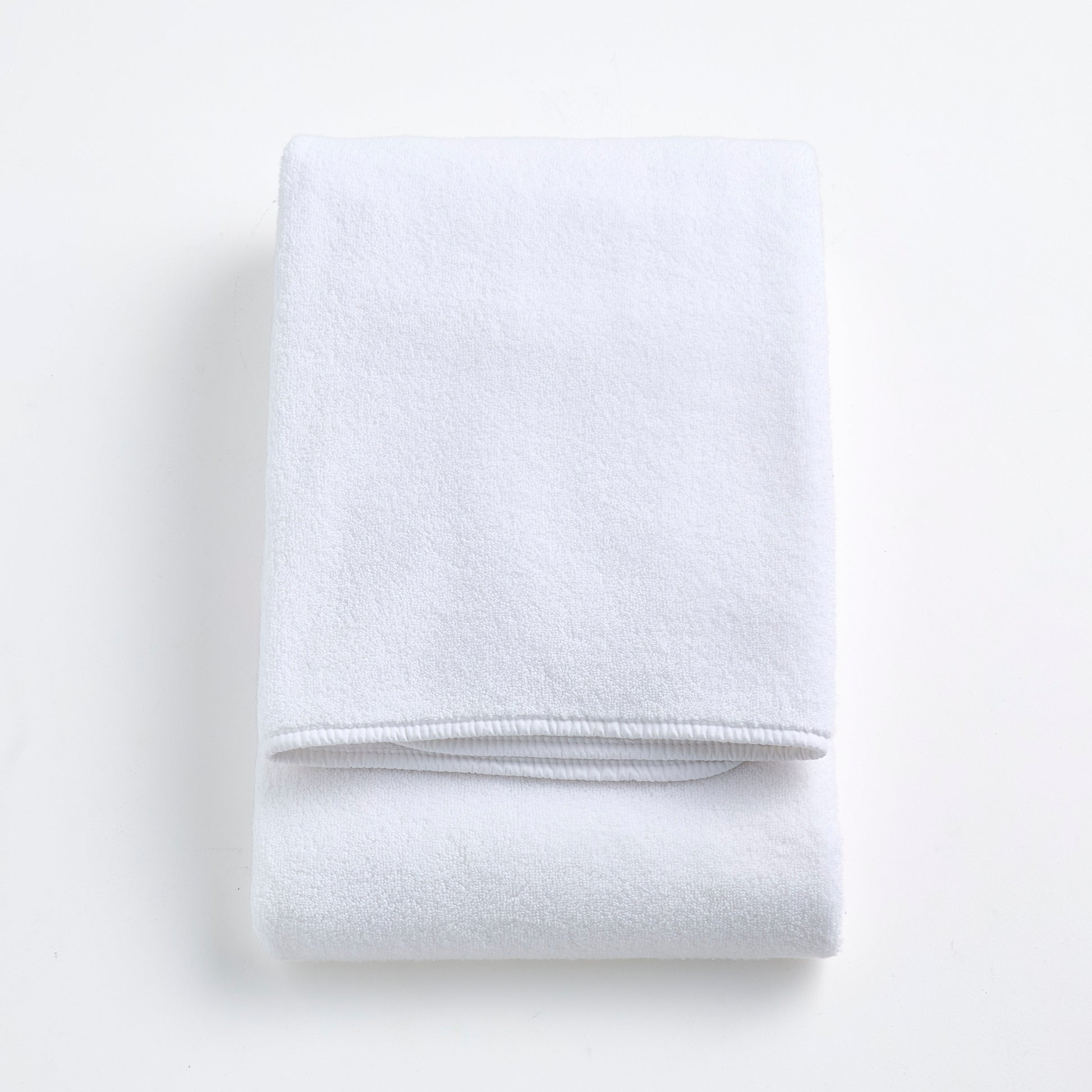 Folded cloud white signature bath towel made of plush, absorbent cotton fabric on a white background.