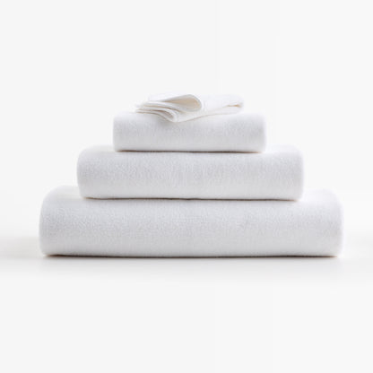 Stack of plush, cloud white zero-twist cotton bath towels with piped edges, made in Portugal.