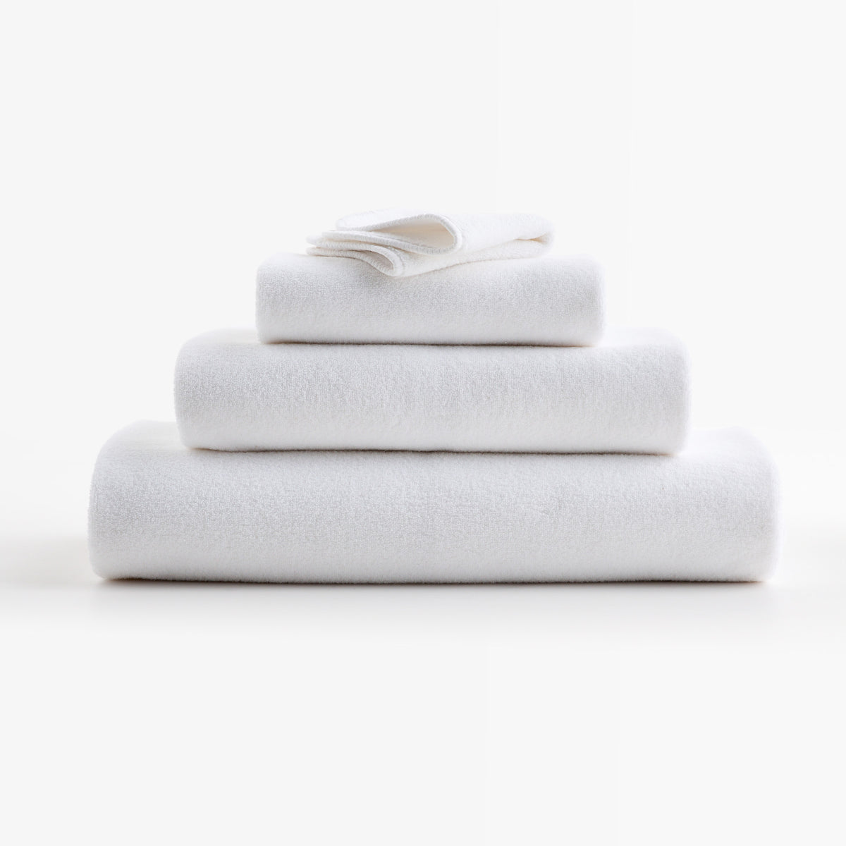 Stack of plush cloud white zero-twist cotton towels with piped edges, made in Portugal.