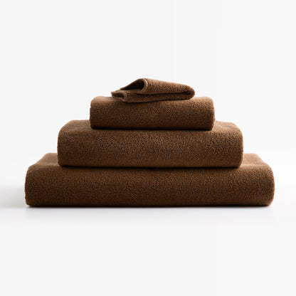 Stack of coffee brown zero-twist cotton bath towels with piped edges from the Hudson Grace Signature Collection.