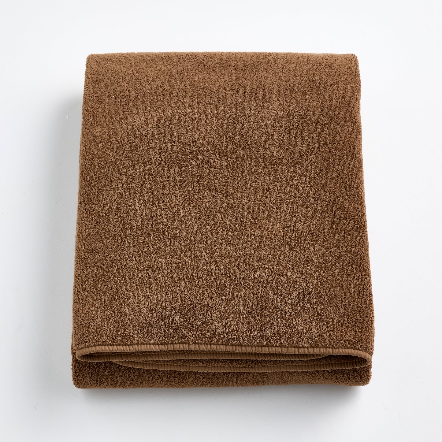 Folded coffee brown cotton bath sheet with a soft, plush texture and finished hem on a white background.