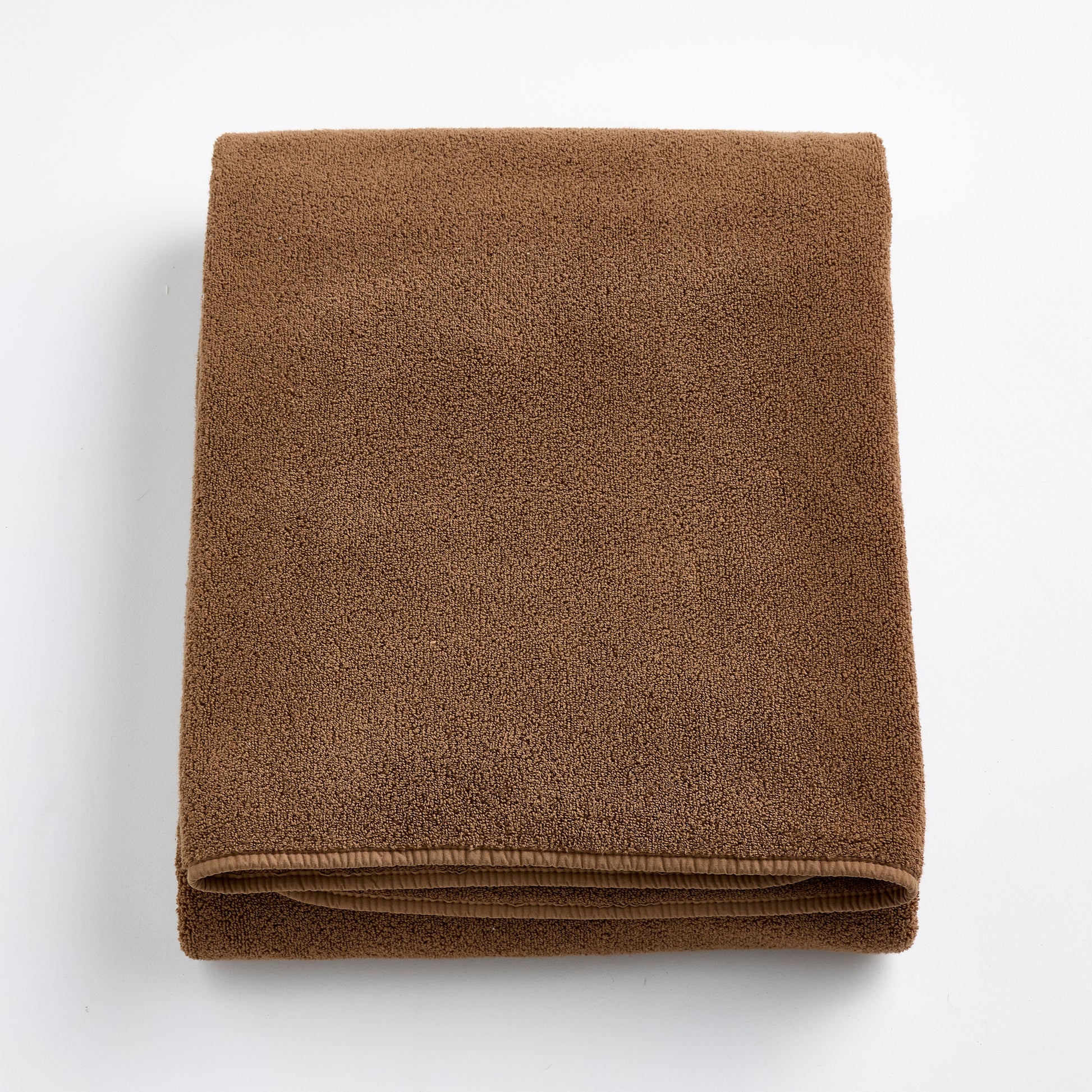 Folded coffee brown cotton bath sheet with a soft, plush texture and finished hem on a white background.