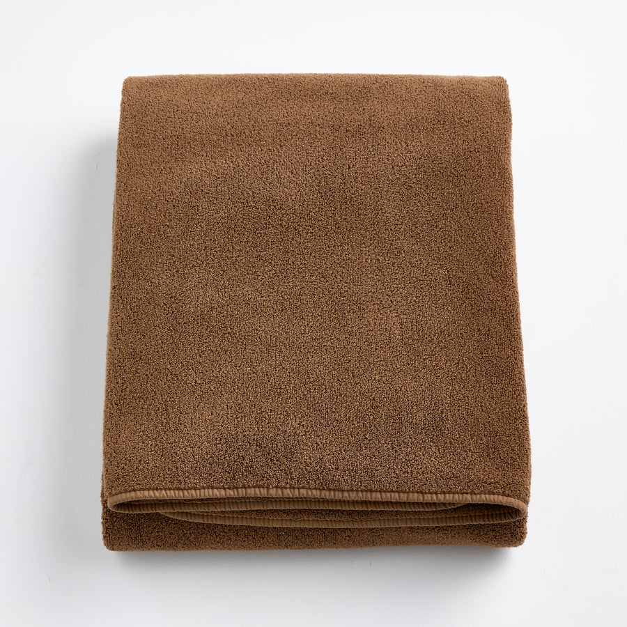 Folded coffee brown cotton bath sheet with a soft, plush texture and finished hem on a white background.
