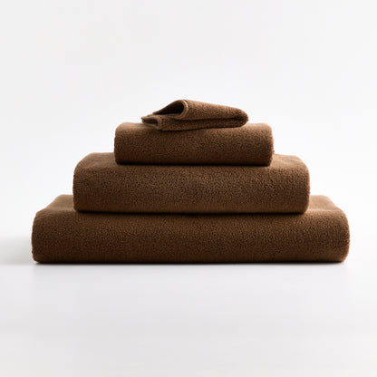 Stack of coffee brown HG Signature cotton towels with piped edges on a white background.