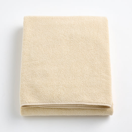 Folded creme brulee signature bath sheet in plush, textured cotton terry fabric on a white background.