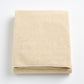 Folded creme brulee signature bath sheet in plush, textured cotton terry fabric on a white background.
