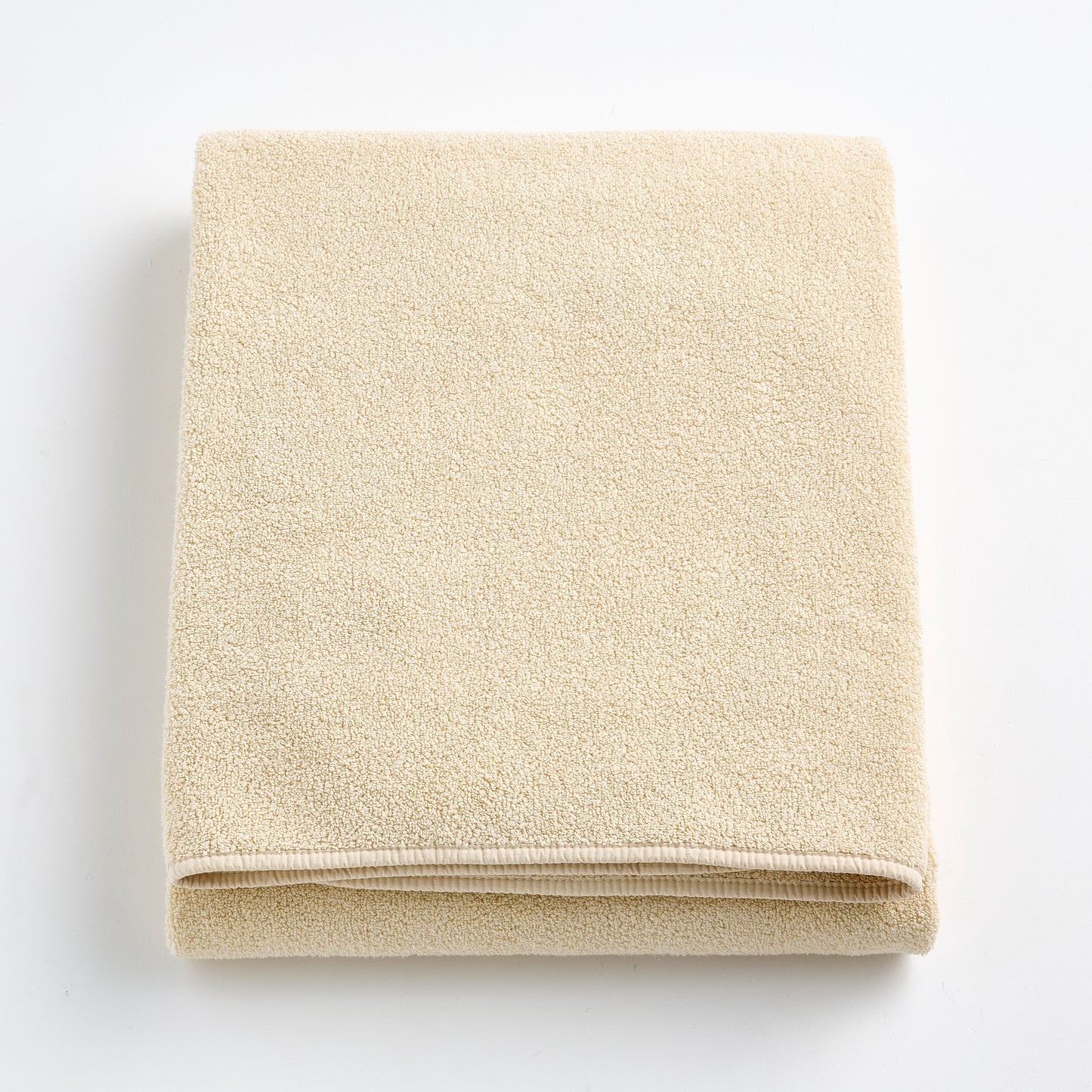 Folded creme brulee signature bath sheet in plush, textured cotton terry fabric on a white background.