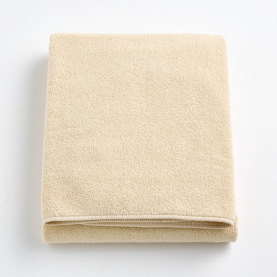 Folded creme brulee signature bath sheet in plush, textured cotton terry fabric on a white background.