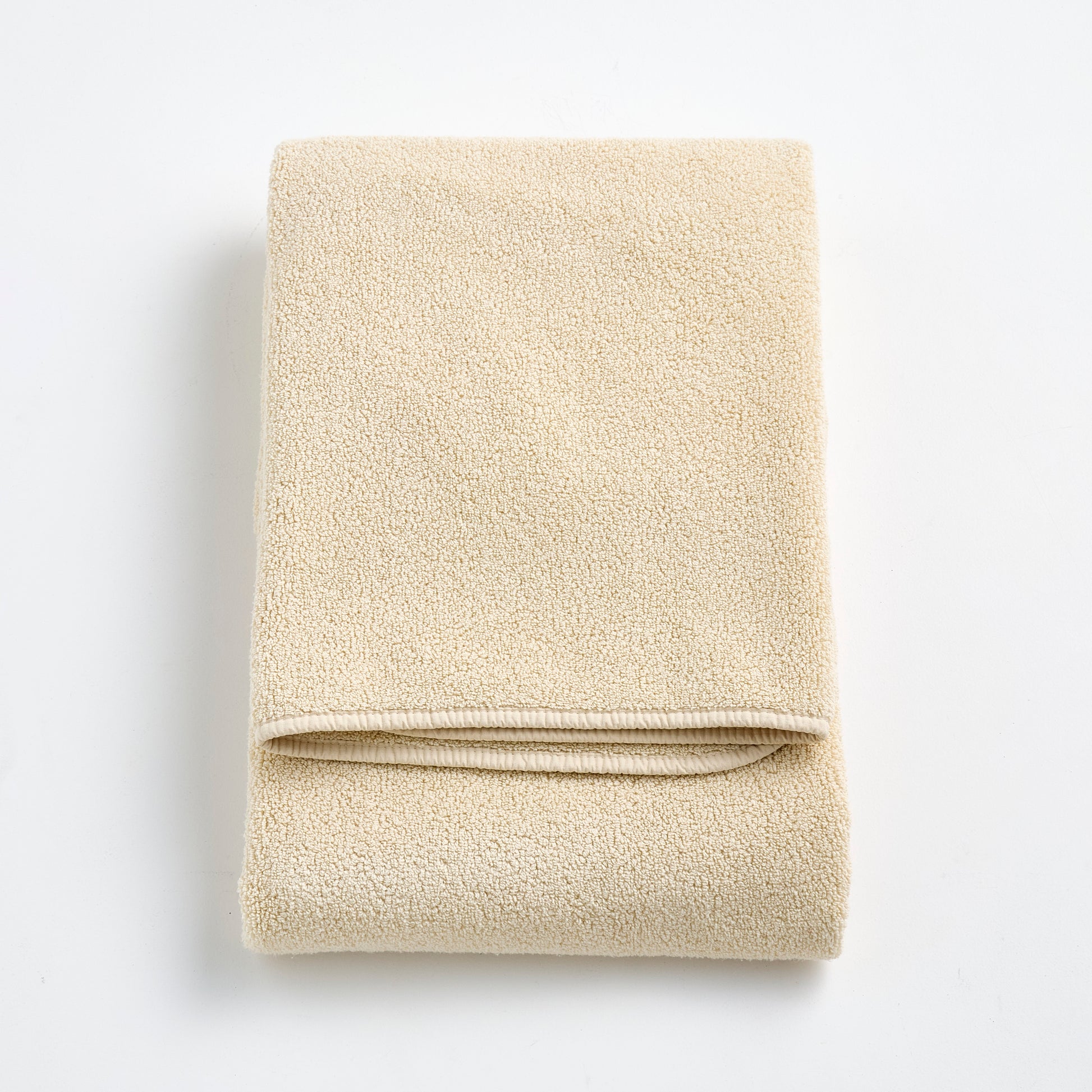 Folded Signature bath towel in creme brulee beige with a plush, textured cotton weave and finished edges.