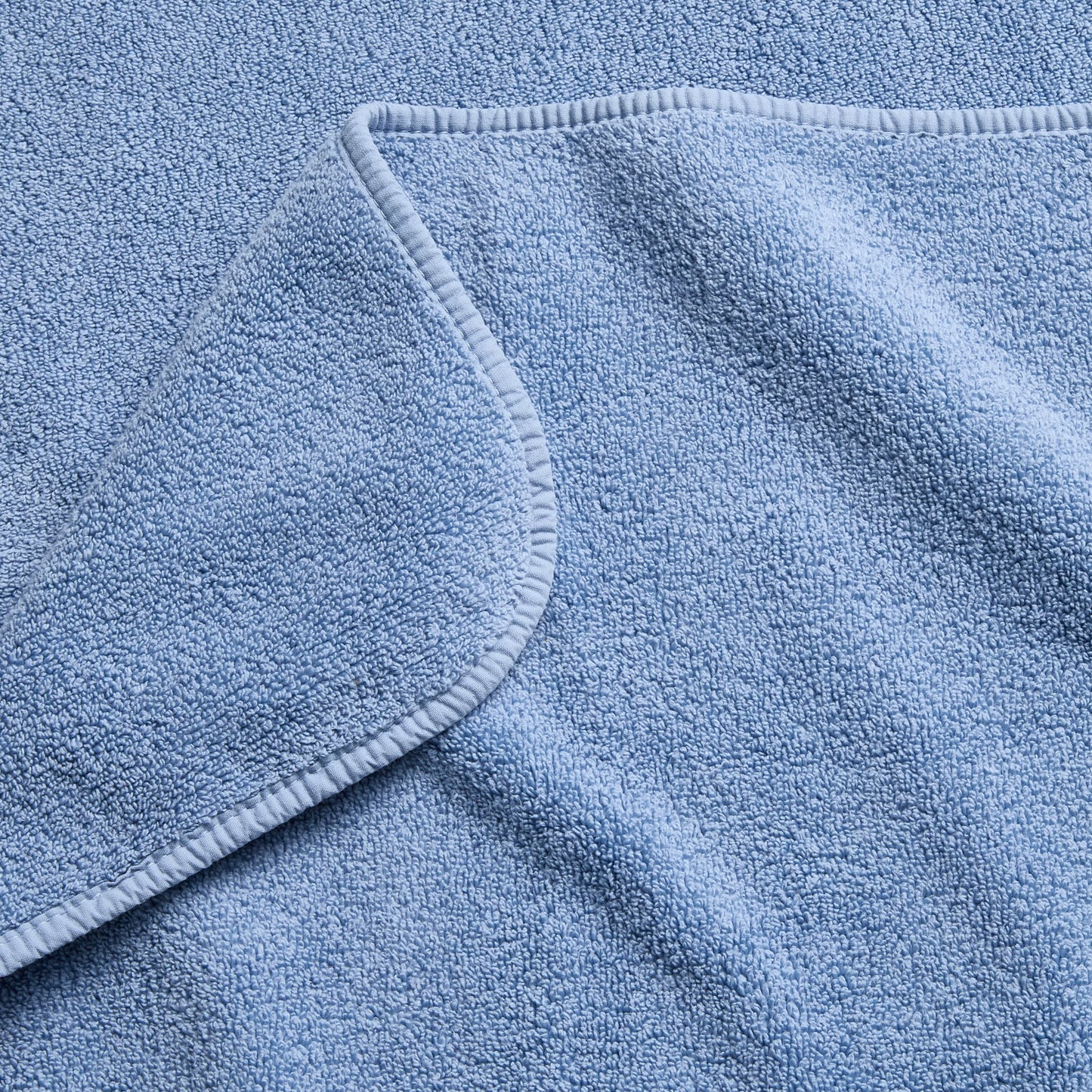 Close-up of a plush denim blue cotton bath sheet with a folded corner and finished stitched hem.