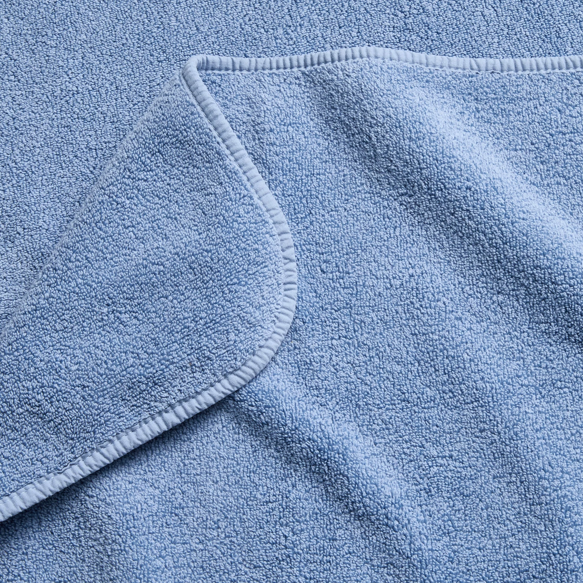 Close-up of a plush denim blue cotton bath sheet with a folded corner and finished stitched hem.