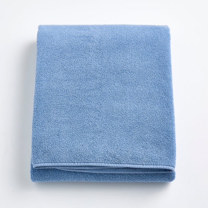Folded denim blue Signature bath sheet in plush, absorbent cotton terry fabric with a clean hemmed edge.