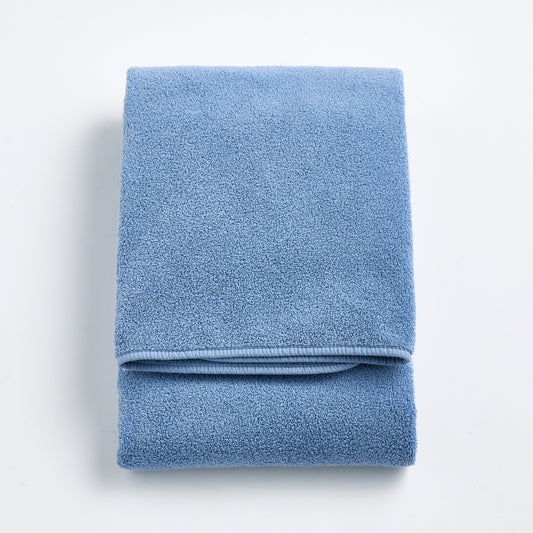 Folded denim blue Signature bath towel with a plush, textured cotton weave on a white background.