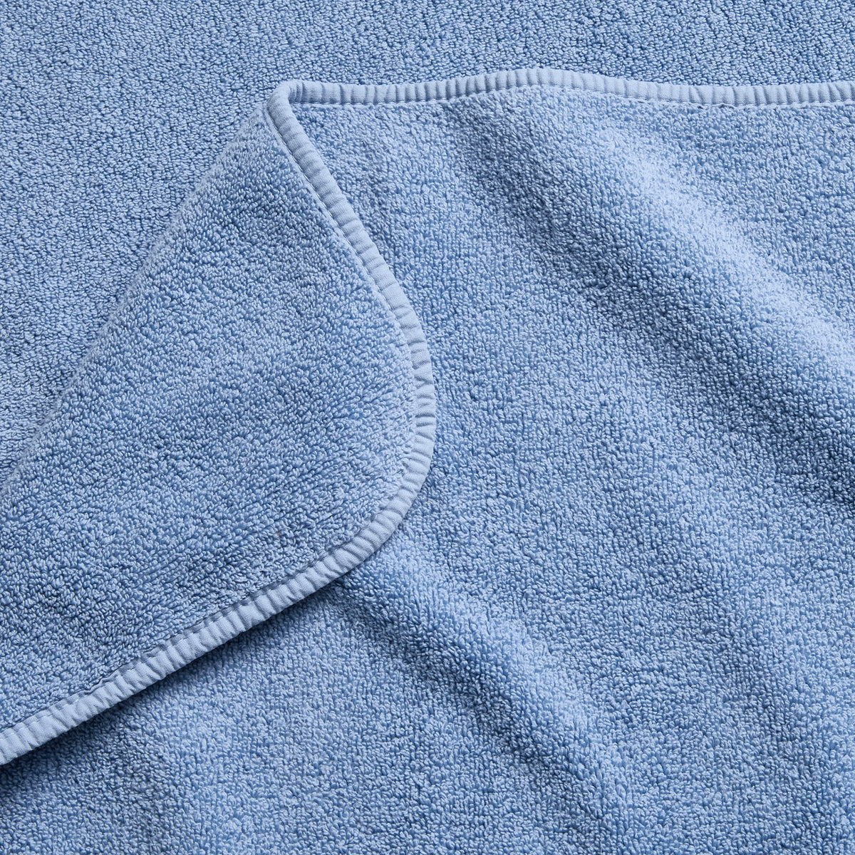Close-up of a plush denim blue cotton bath sheet with a folded corner and finished stitched hem.