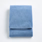Folded denim blue Signature bath towel with a plush, textured cotton weave on a white background.