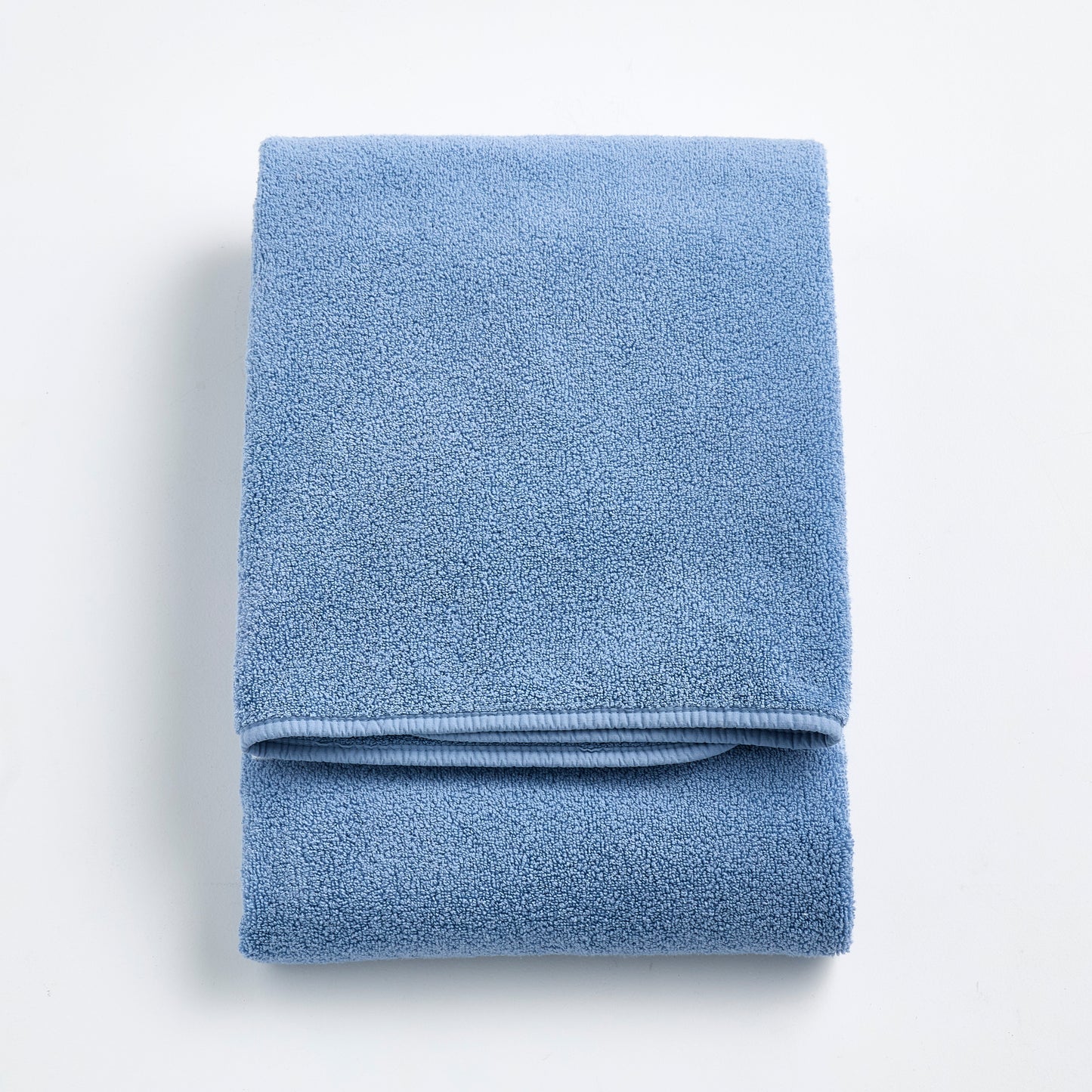 Folded denim blue Signature bath towel with a plush, textured cotton weave on a white background.