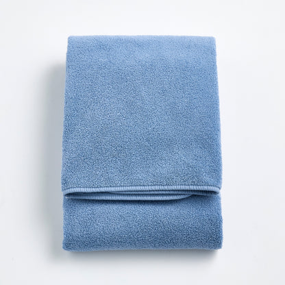Folded denim blue Signature bath towel with a plush, textured cotton weave on a white background.