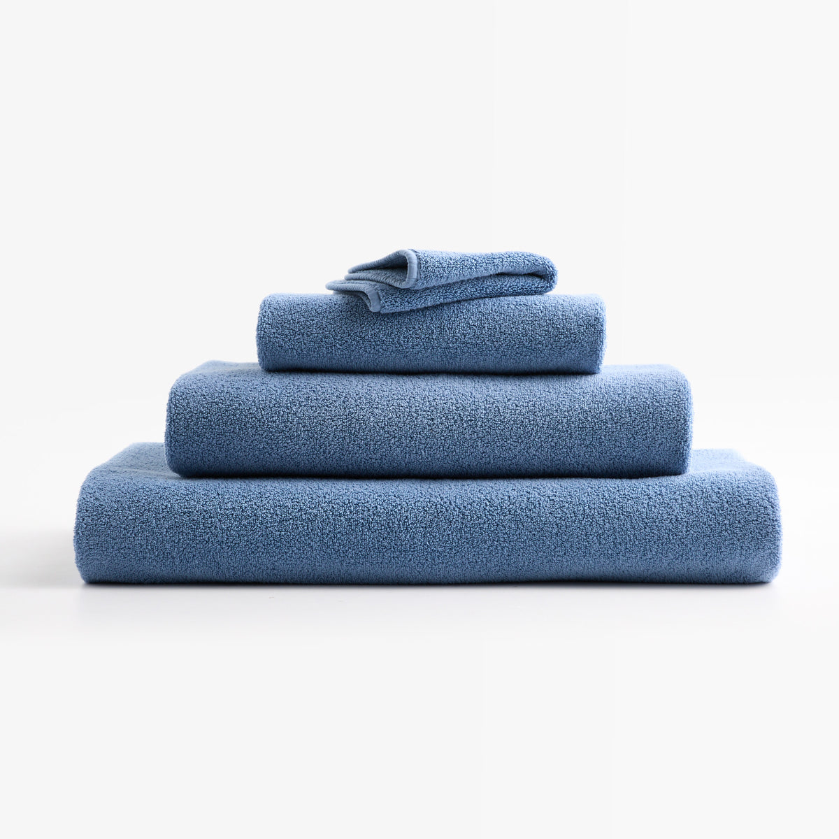 Stack of plush denim blue zero-twist cotton hand towels with piped edges, made in Portugal.