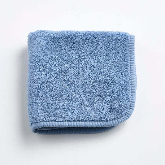 Folded denim blue cotton terry washcloth with a matching stitched border on a white background.