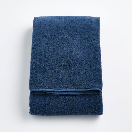 Folded indigo blue Signature bath towel with a soft, plush cotton texture and finished hem on a white background.