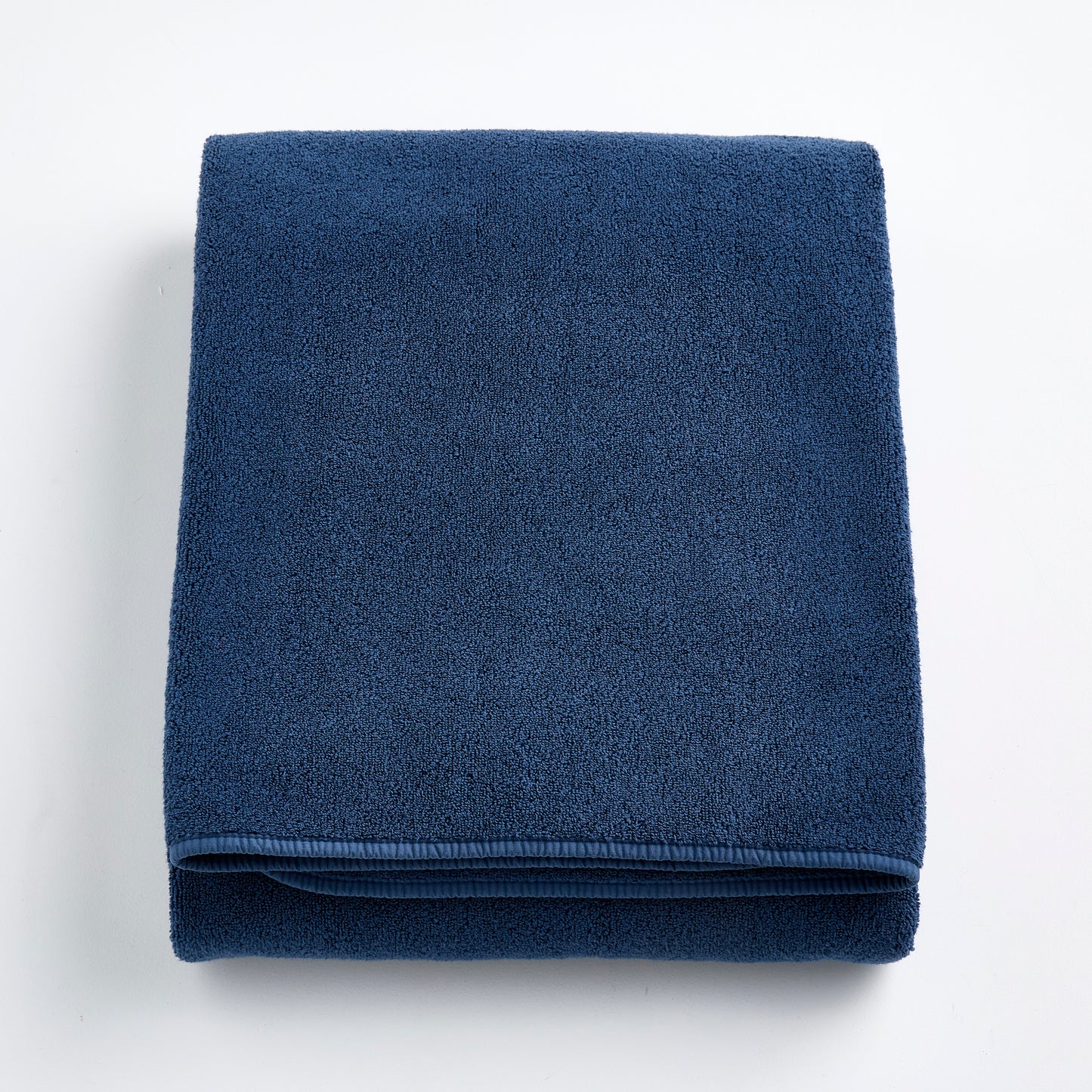 Folded indigo blue Signature bath sheet made of plush, absorbent cotton terry fabric.