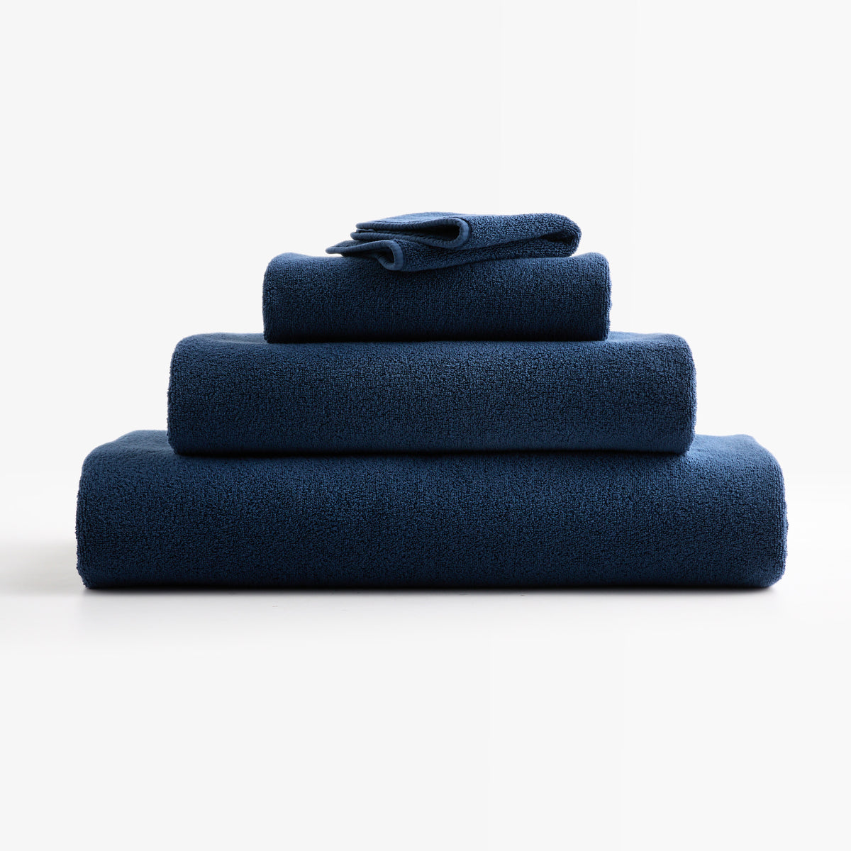 Stack of folded HG Signature indigo blue zero-twist cotton bath towels with piped edges.