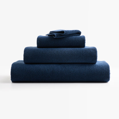 Stack of folded HG Signature indigo blue zero-twist cotton bath towels with piped edges.