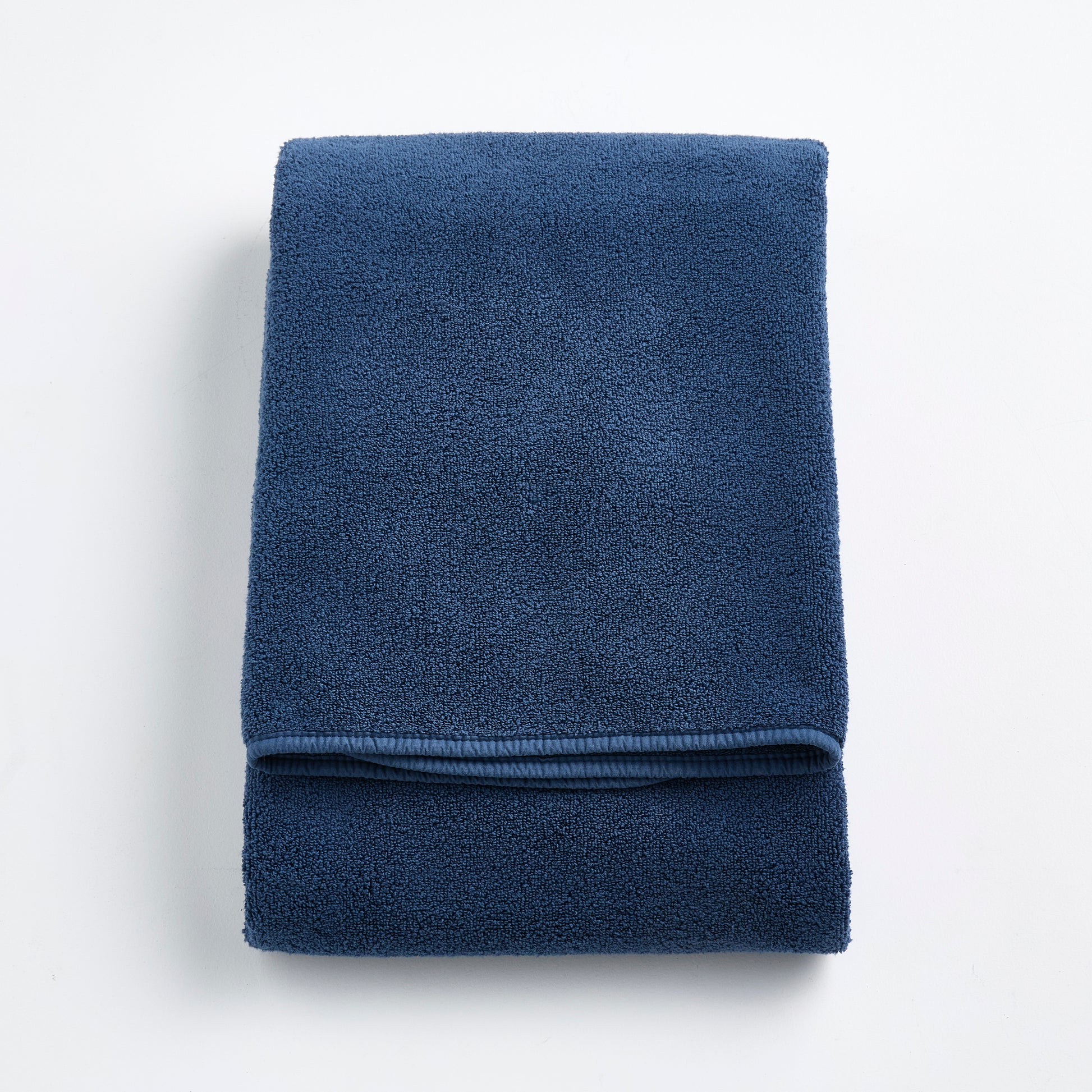 Folded indigo blue Signature bath towel with a soft, plush cotton texture and finished hem on a white background.