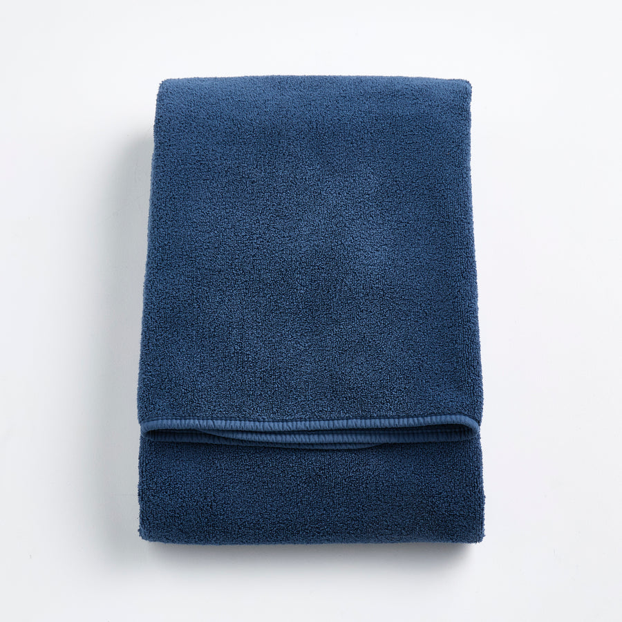 Folded indigo blue Signature bath towel with a soft, plush cotton texture and finished hem on a white background.