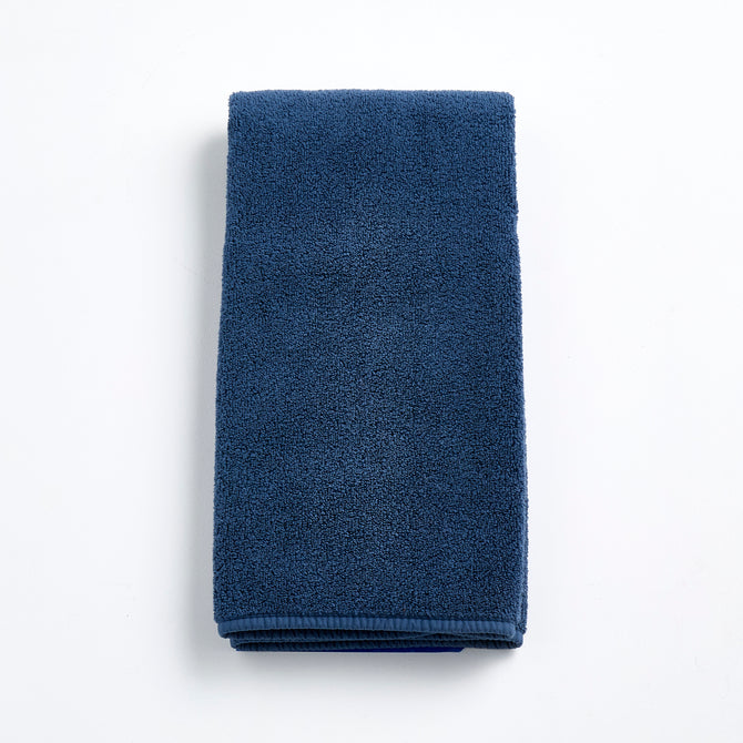 Folded indigo blue hand towel made of soft, textured cotton terry cloth on a white background.