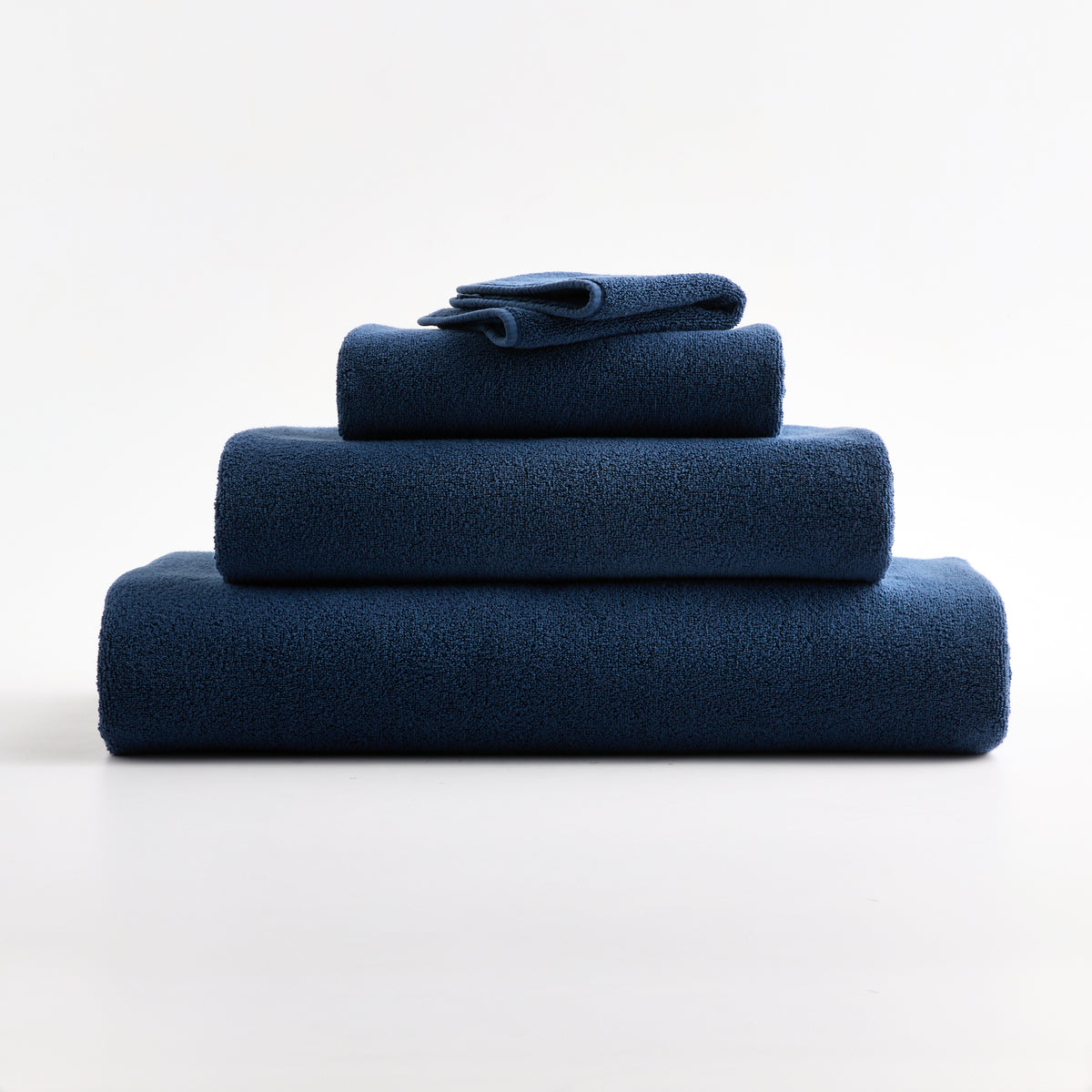 Stack of indigo blue zero-twist cotton washcloths and towels with piped edges.